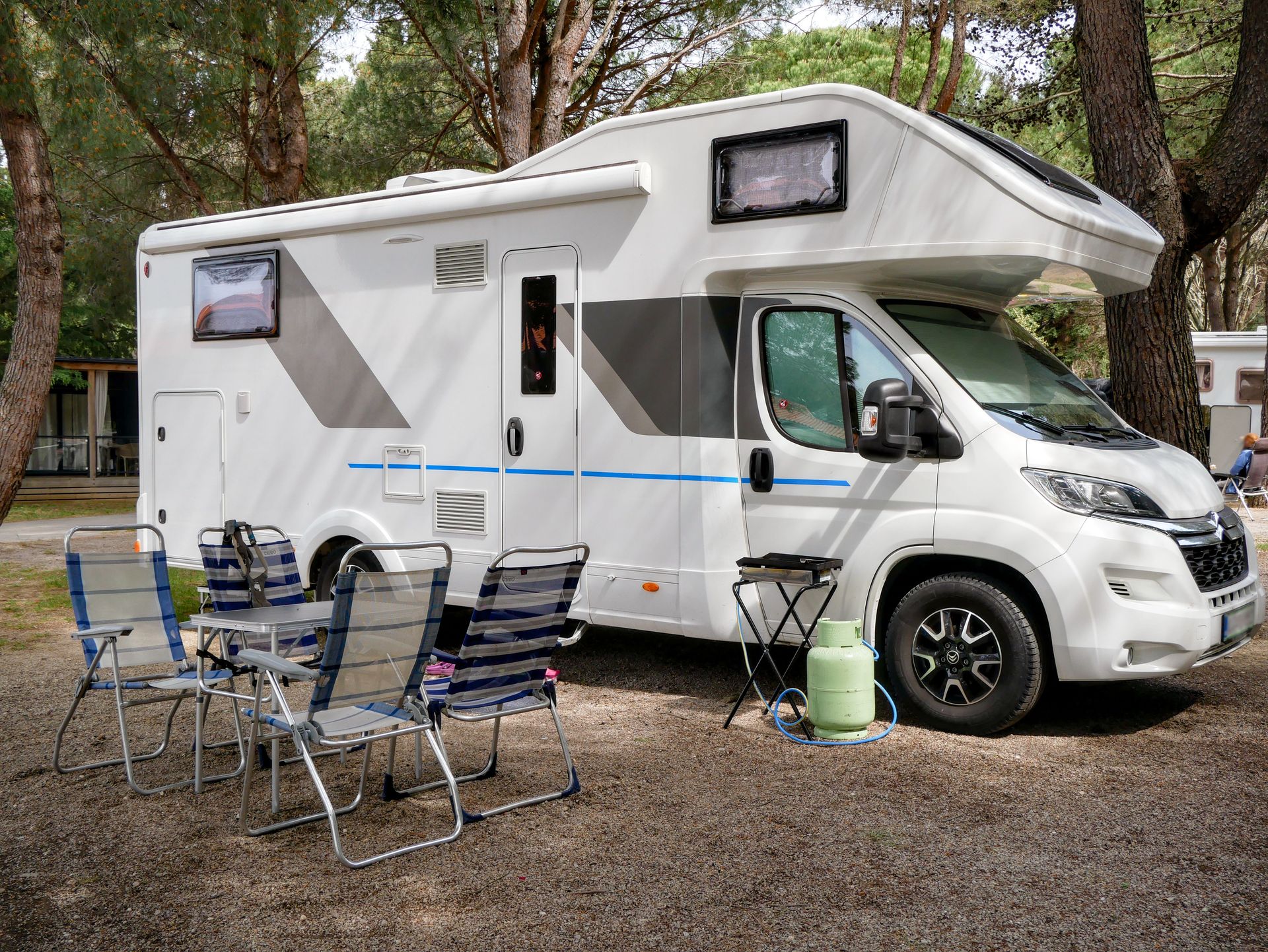A modern RV parked in a forest campsite with outdoor seating, ideal for family adventures.