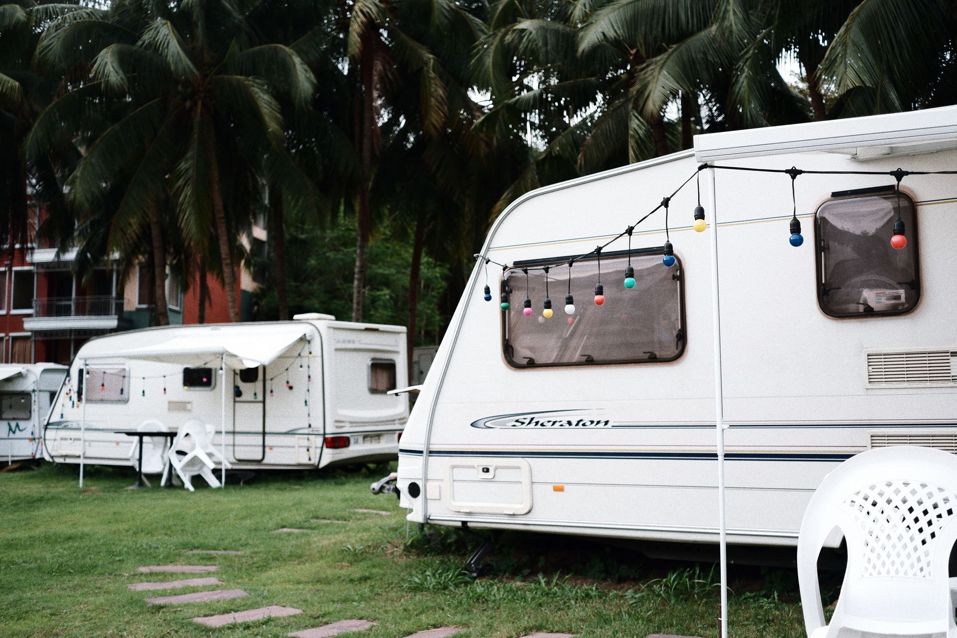 Relaxing caravan camping site under palm trees with outdoor seating and festive lights.